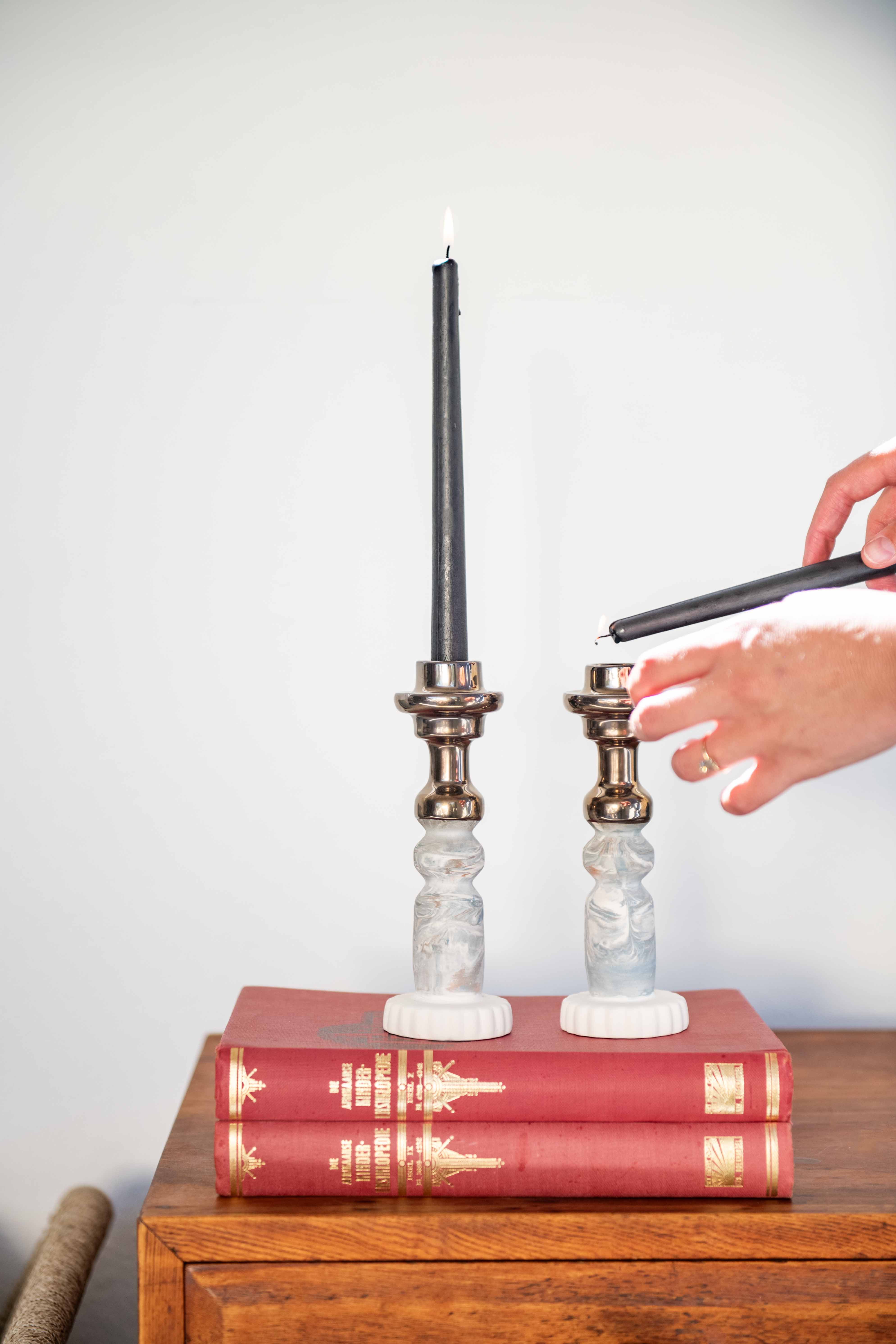 two Rialheim Candle stick holders with blue and white clay and bronze tops on red books with a white back ground