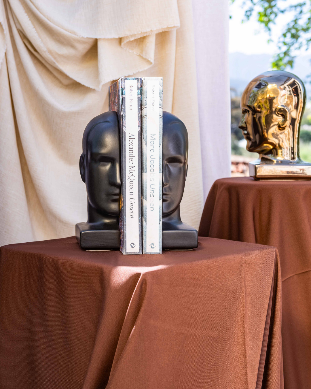 Decorative bookends shaped like human heads on a table with books and a gold head sculpture.