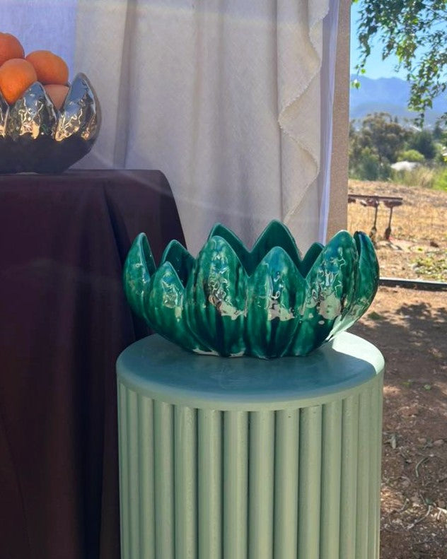Decorative green vase on a cylindrical stand outdoors with a blurred background