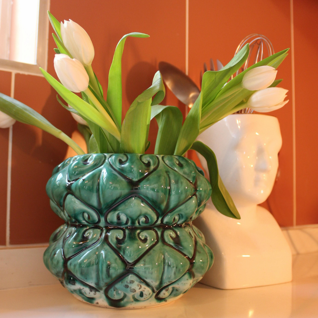 Turquoise ceramic vase with decorative patterns containing white tulips, placed on a surface with a blurred background From Rialheim 