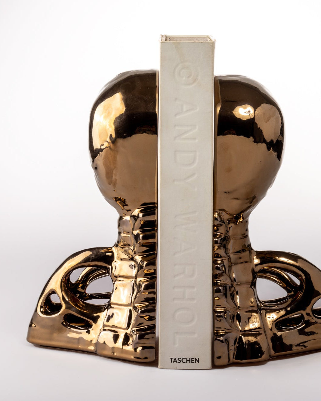 Gold human skull and spine bookend with 'Taschen' branding on a white background