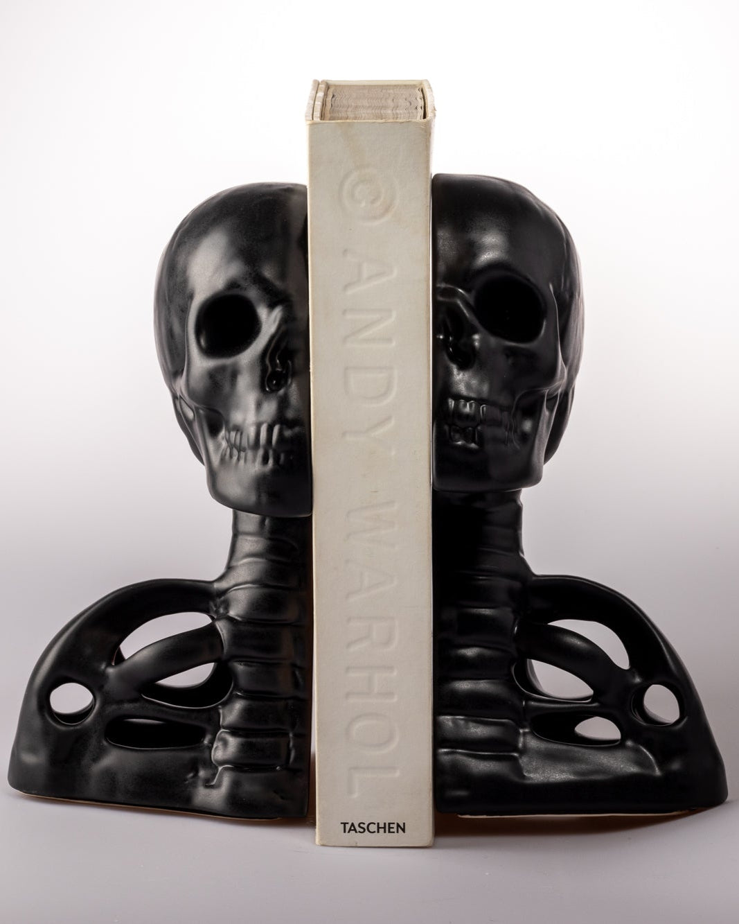 Black skull-shaped bookends with a book between them on a white background