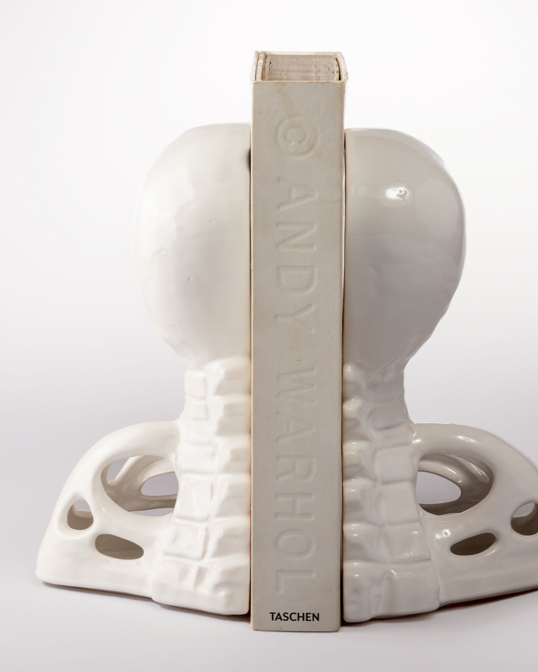 White ceramic human skull end spine bookends with 'Andy Warhol' book inside on a white background