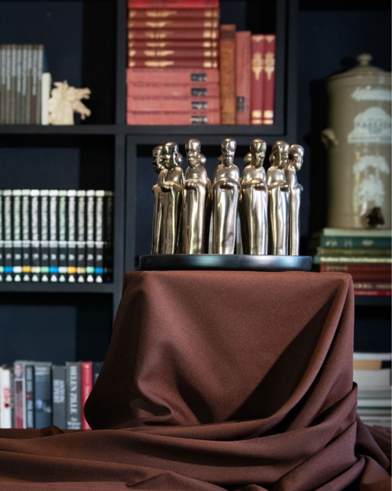 Decorative setup with gold statues on a brown cloth in front of a bookshelf.