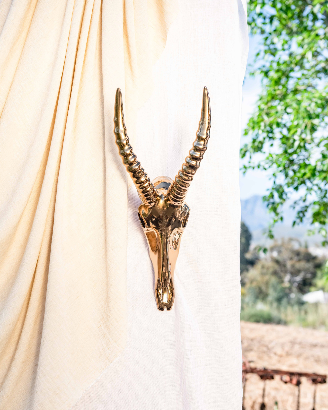 Decorative brass antelope head mounted on a white curtain with outdoor scenery in the background