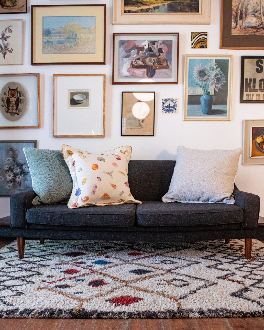 Gray sofa with a light blue pillow against a wall with framed artwork