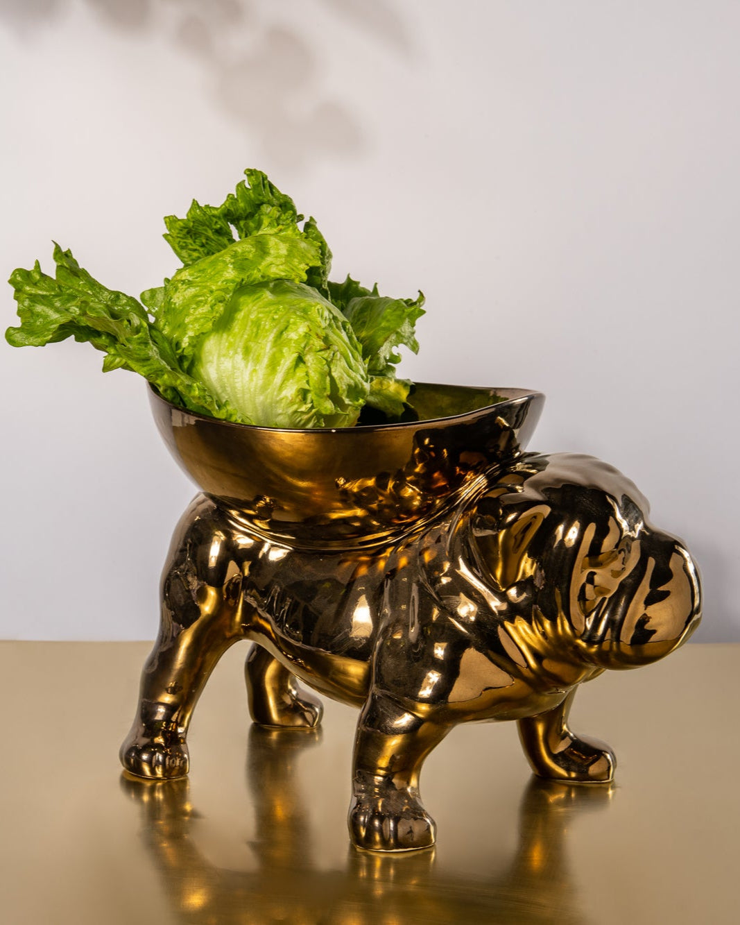Gold bulldog-shaped bowl with green leaves on a white background