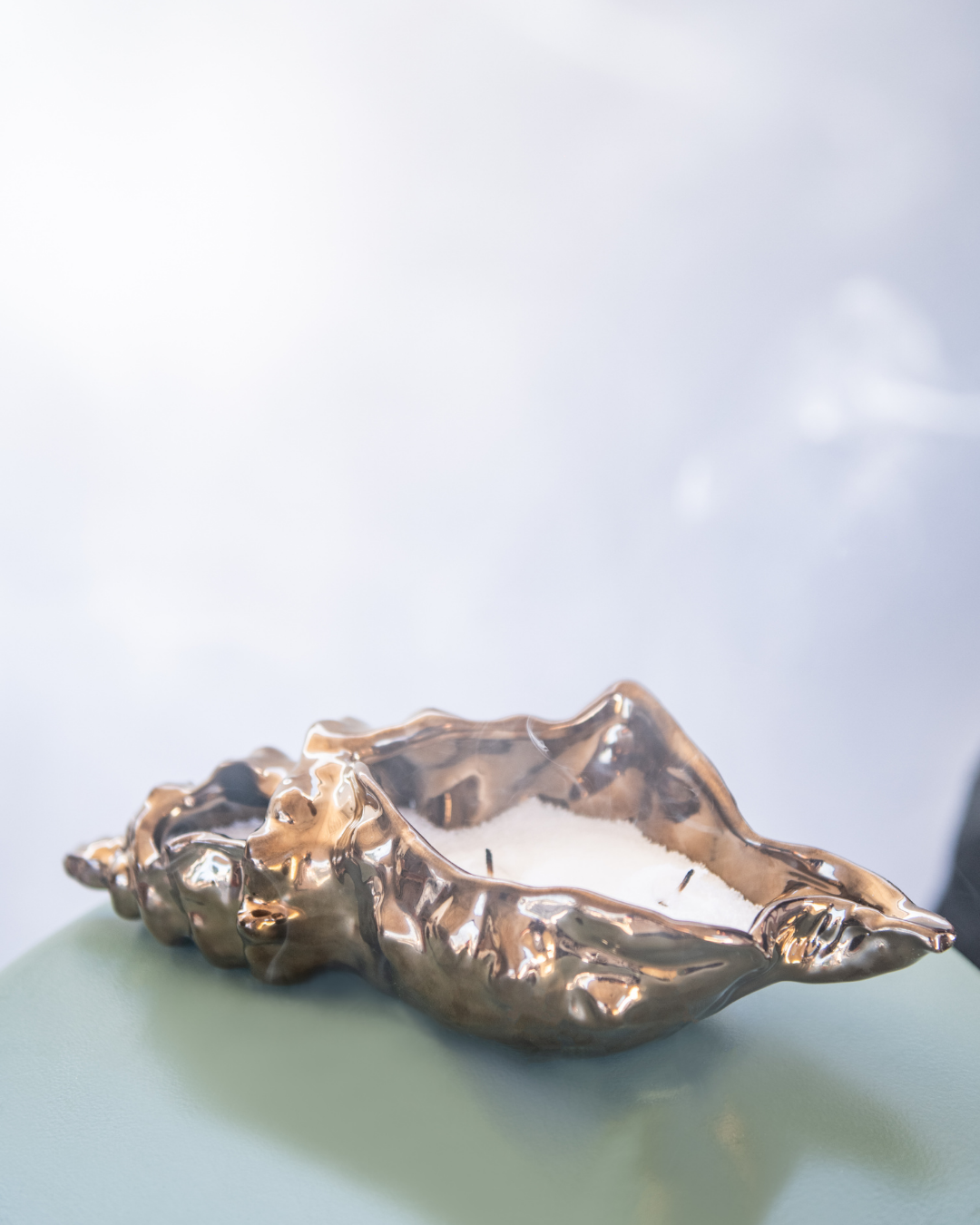 Gold shell-shaped candle holder on a light blue surface with a blurred background