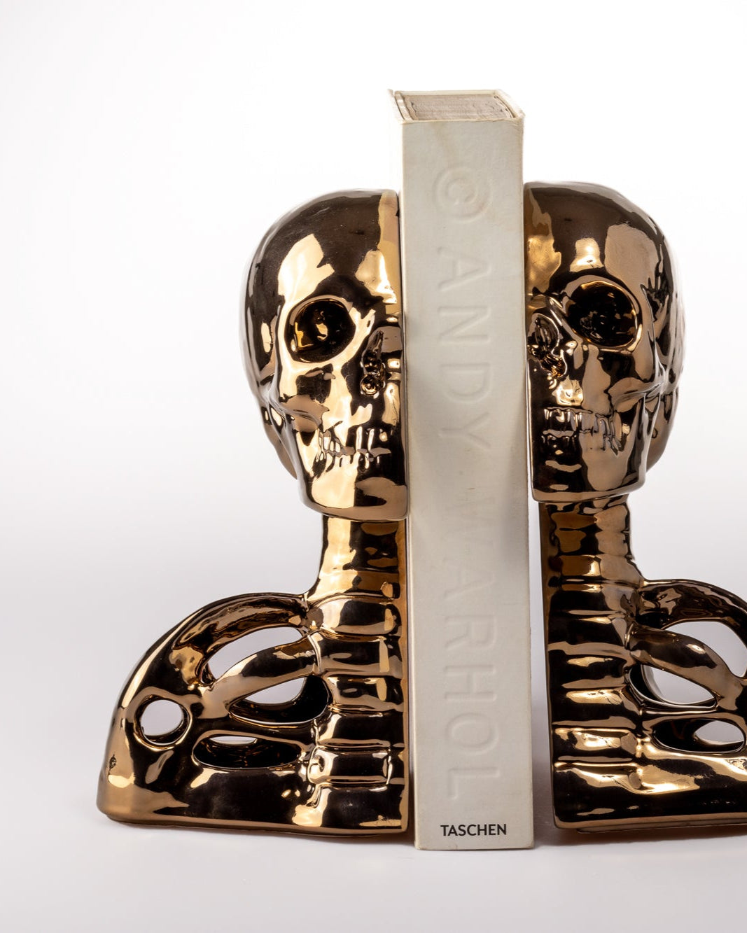Gold skull-shaped bookends with a white book between them on a white background