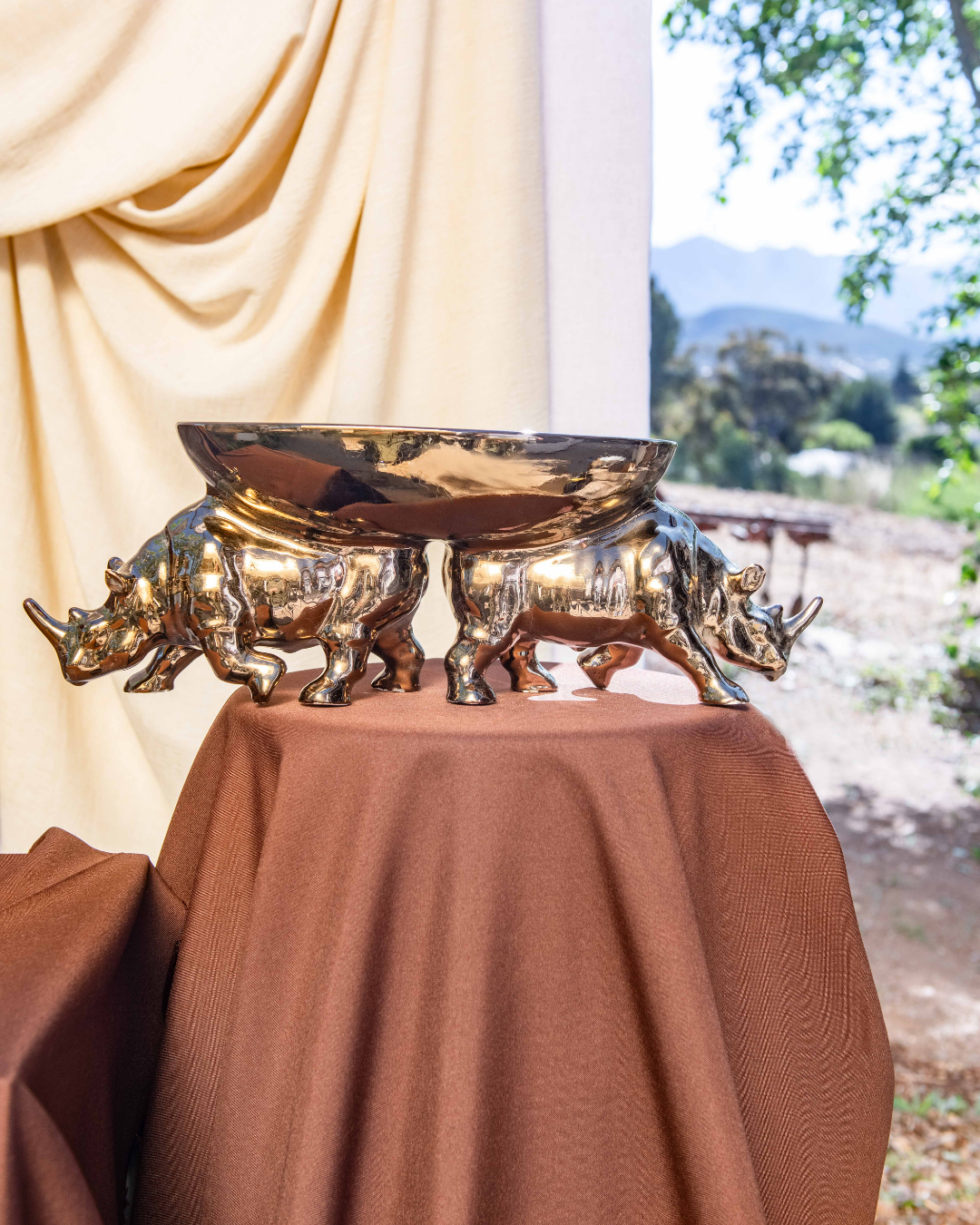 Gold rhinoceros-shaped bowl on a brown tablecloth with a scenic background