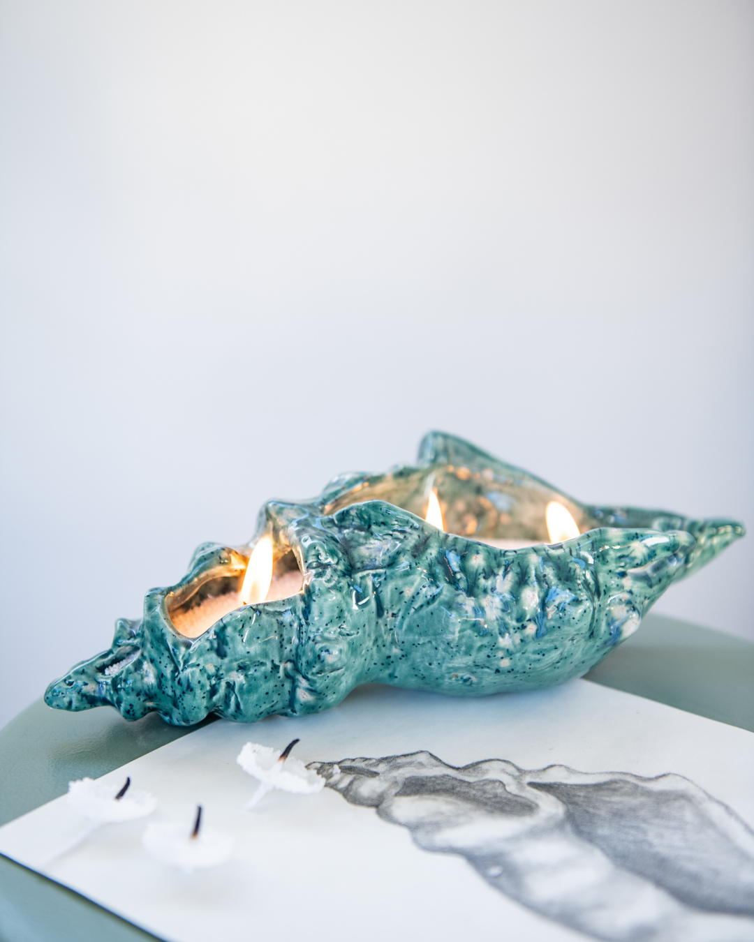 Crystal Glaze shell-shaped candle holder with a lit candle on a light surface.