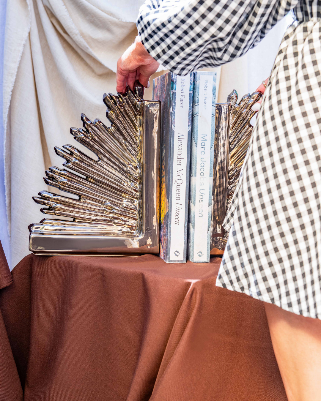 Bronze Crown Bookends on a brown cloth with a person putting books in between the two pieces