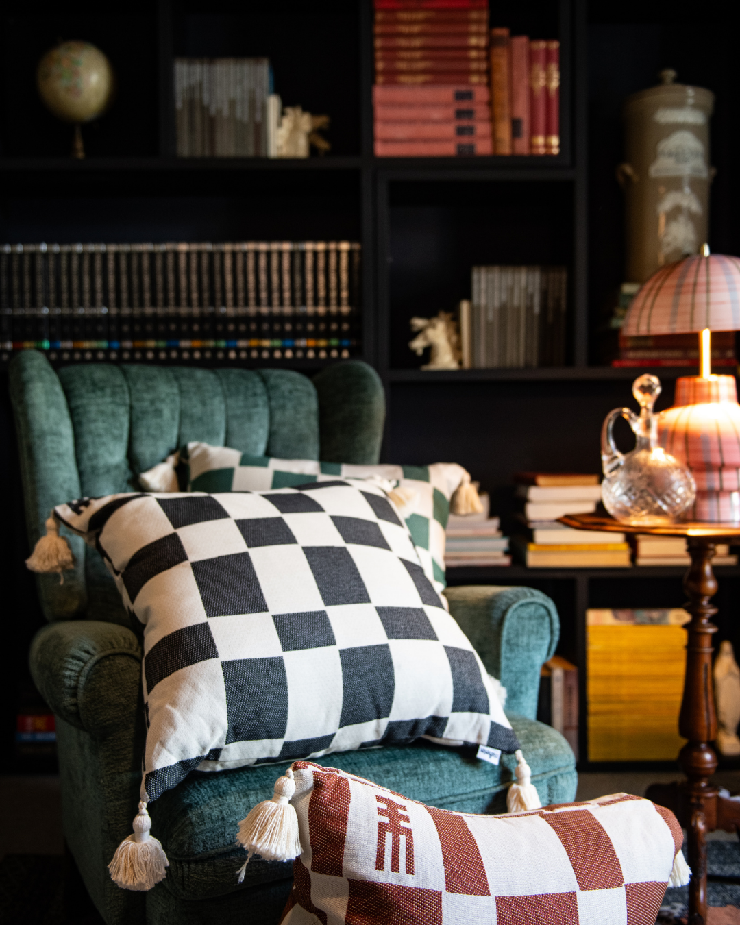Green armchair with checkered cushions in a cozy room with books and decor.