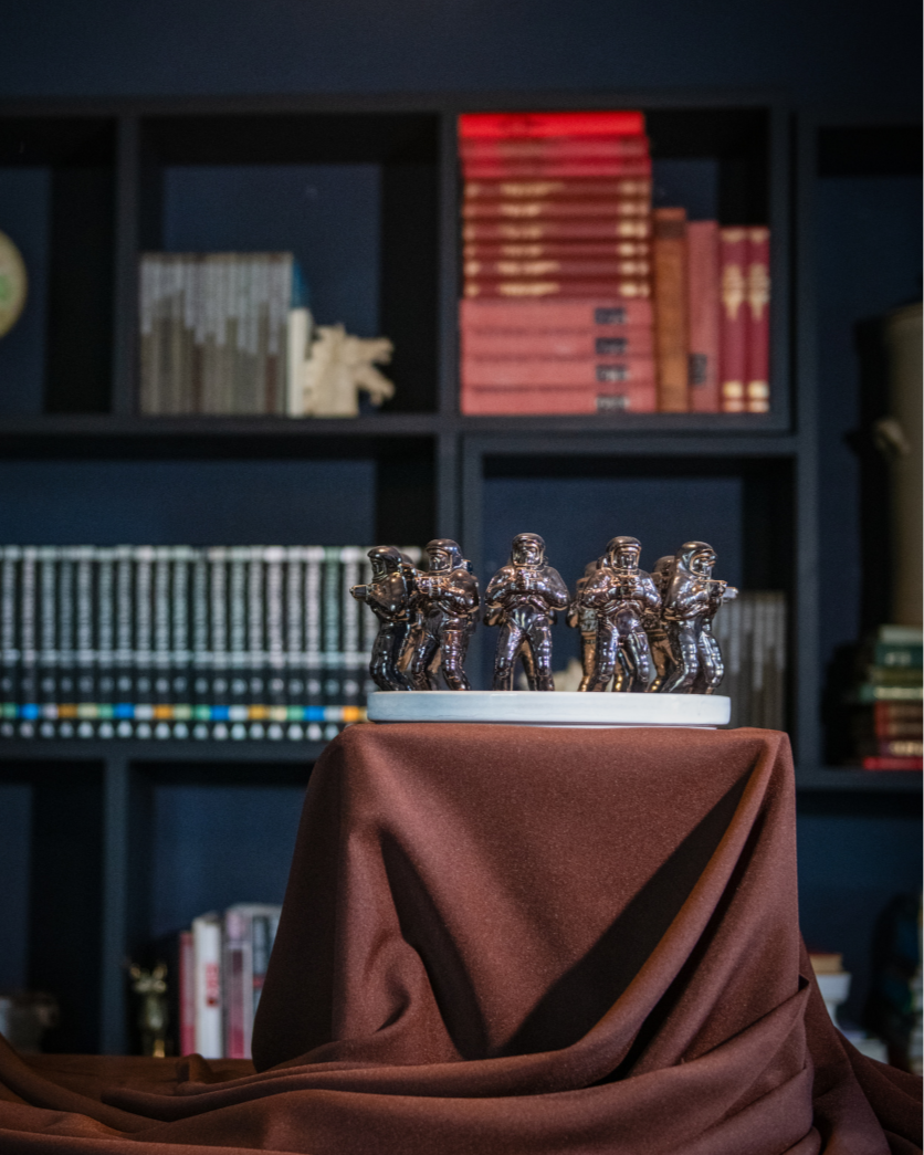 Decorative display of small statues on a tablecloth in front of a bookshelf.