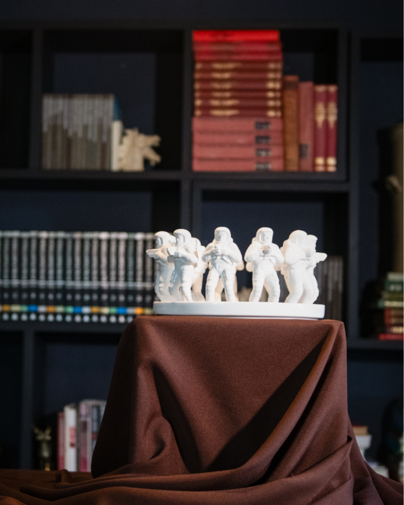 White figurines on a brown cloth with a bookshelf in the background