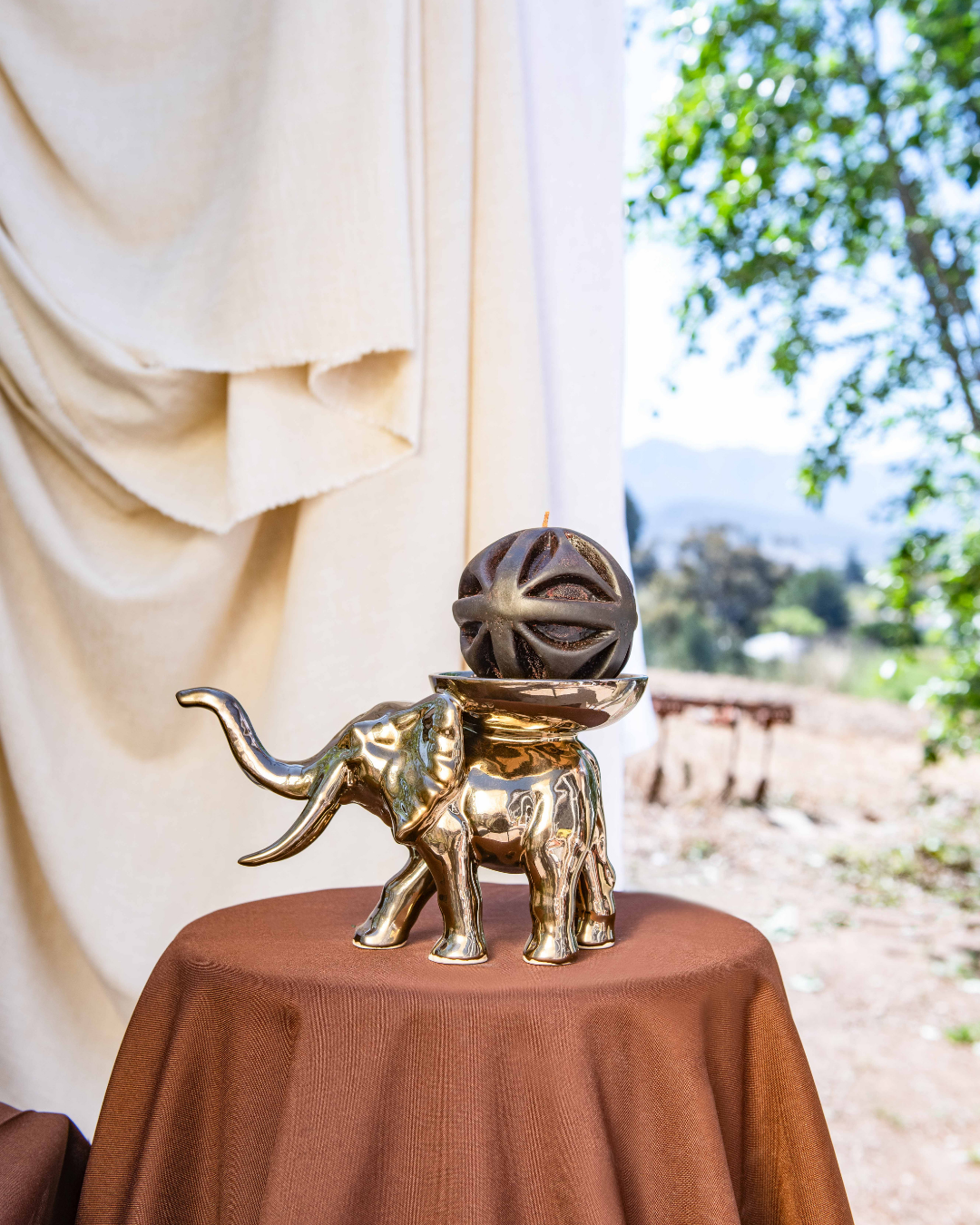 Gold elephant figurine with a sphere sculpted candle on a round table outdoors