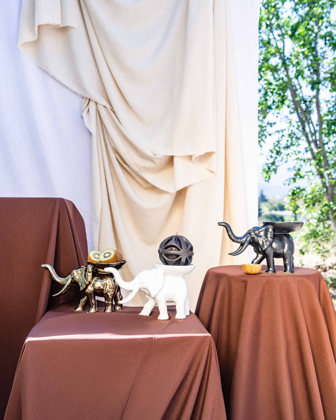 Decorative elephant figurines on a table with a draped curtain and outdoor view in the background