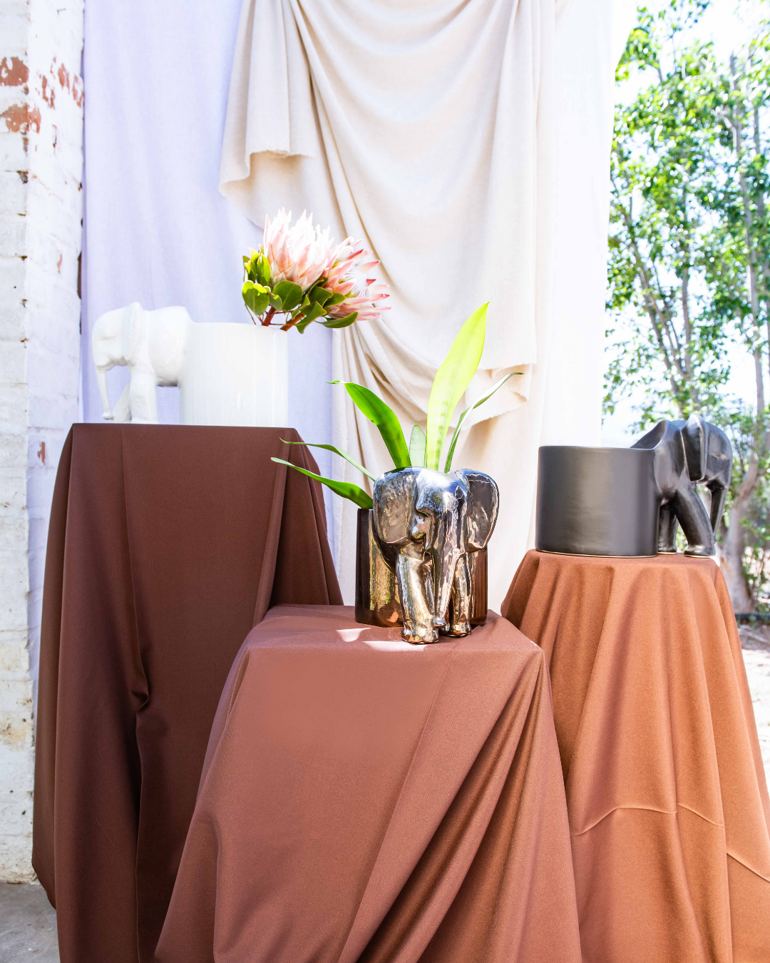 Decorative setup with draped tables, vases, and elephant statues outdoors.