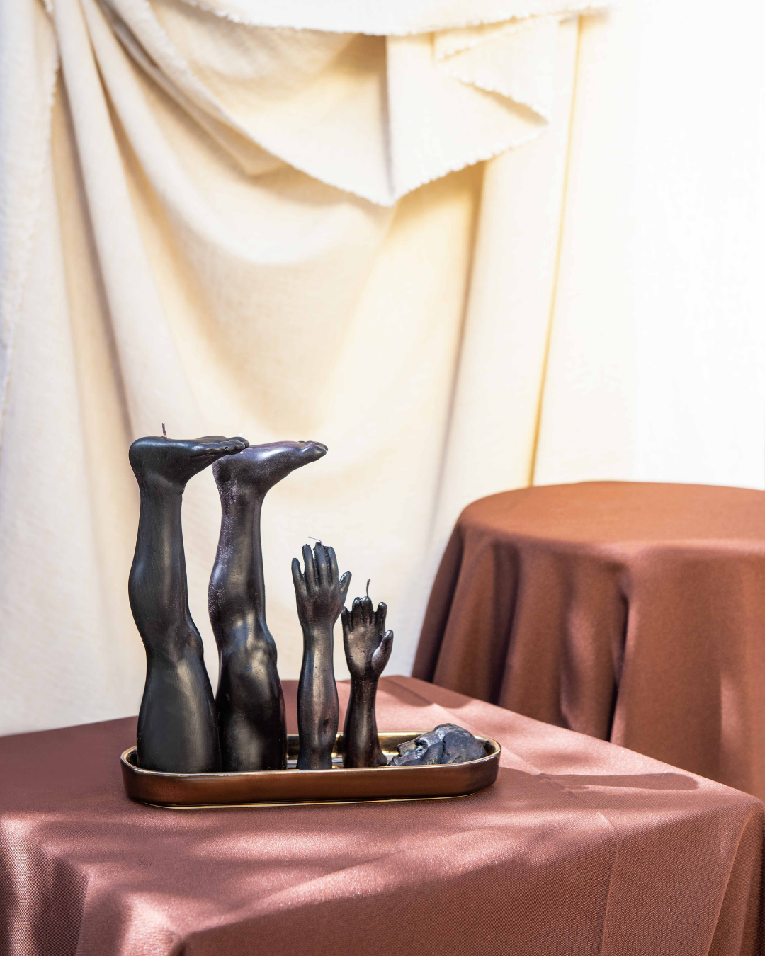 Decorative sculpture of hands and feet on a table with draped fabric in the background