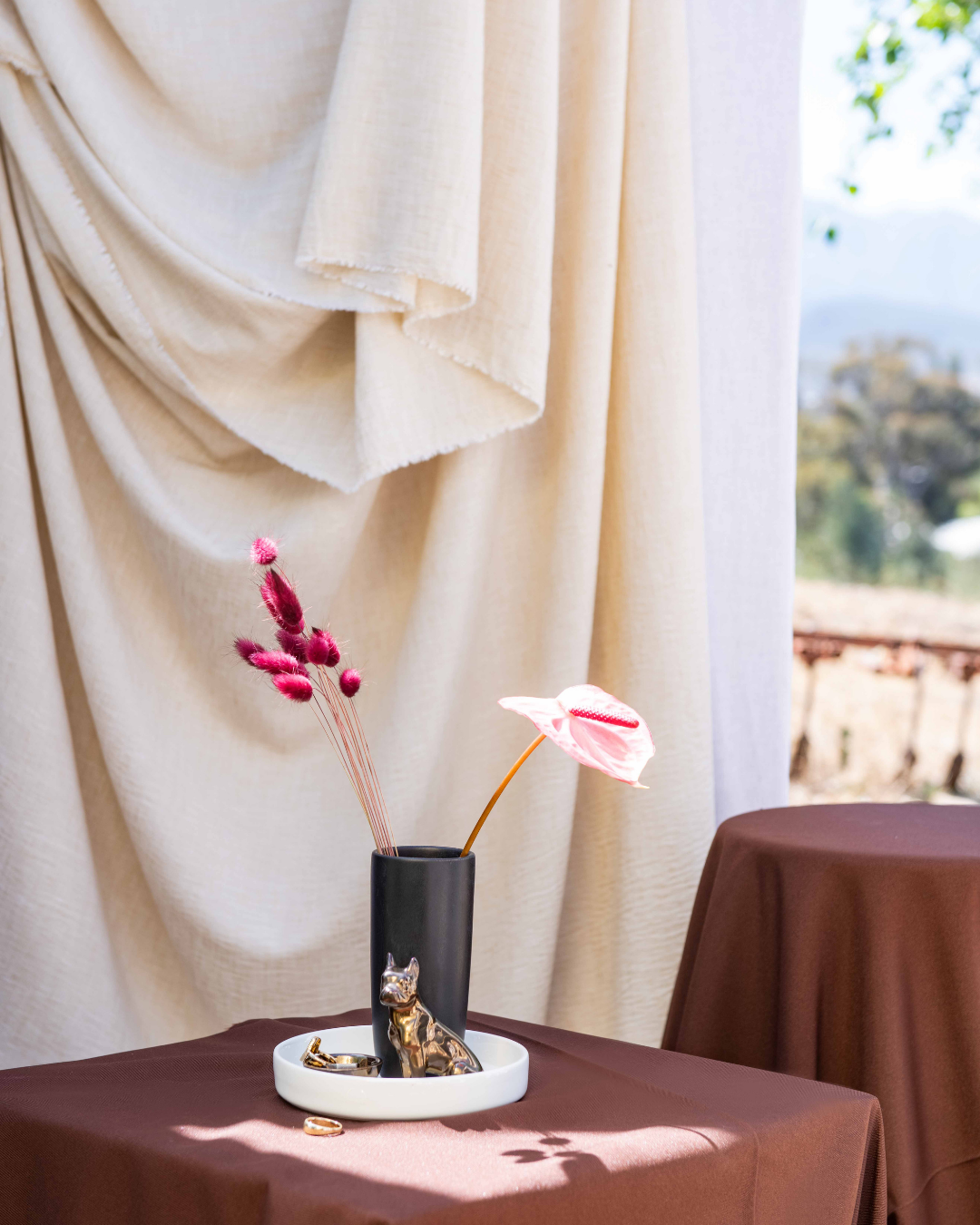 Decorative vase with french Bull dog pink flowers on a table with draped curtains in the background