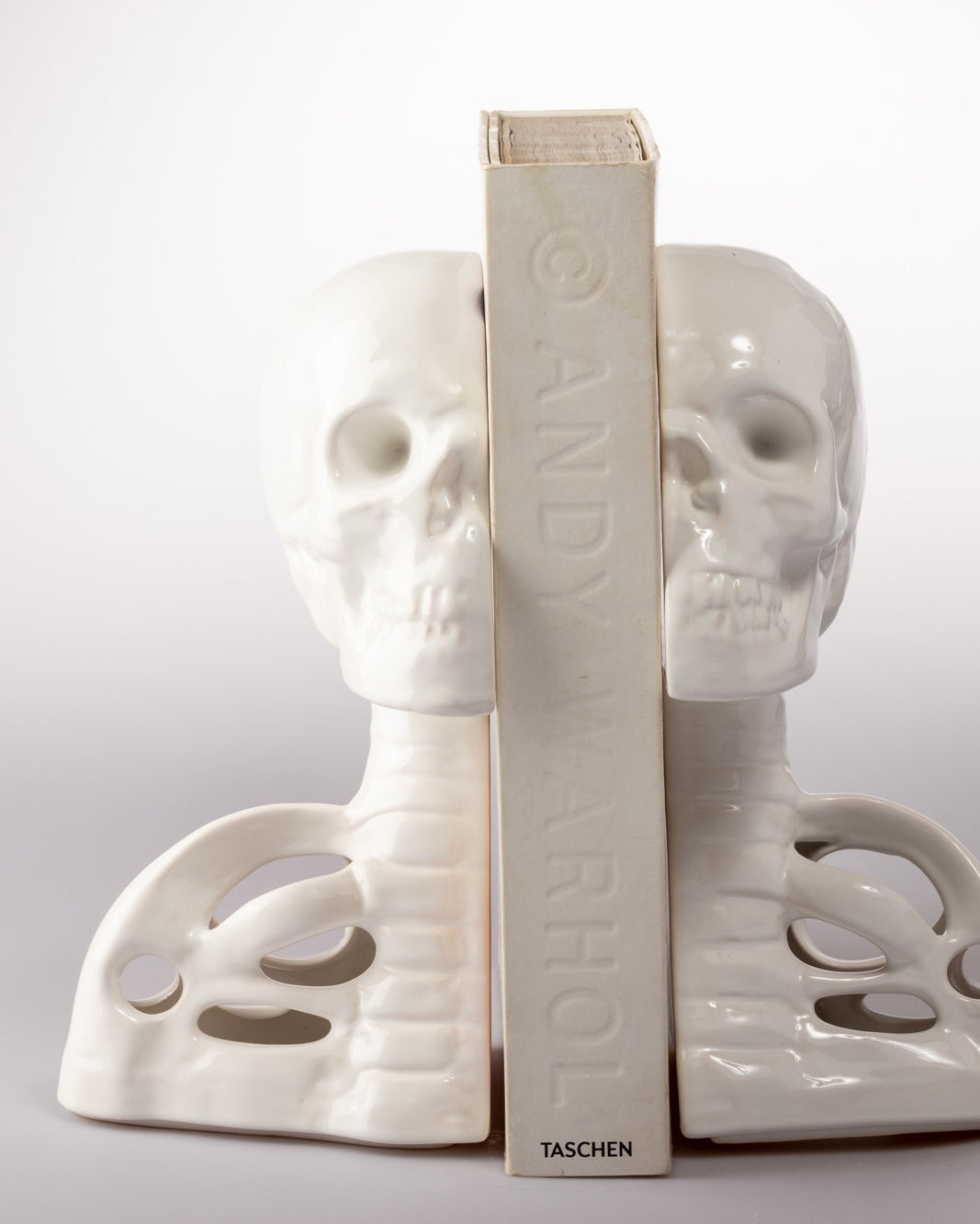 White skull-shaped bookends with a book between them on a white background