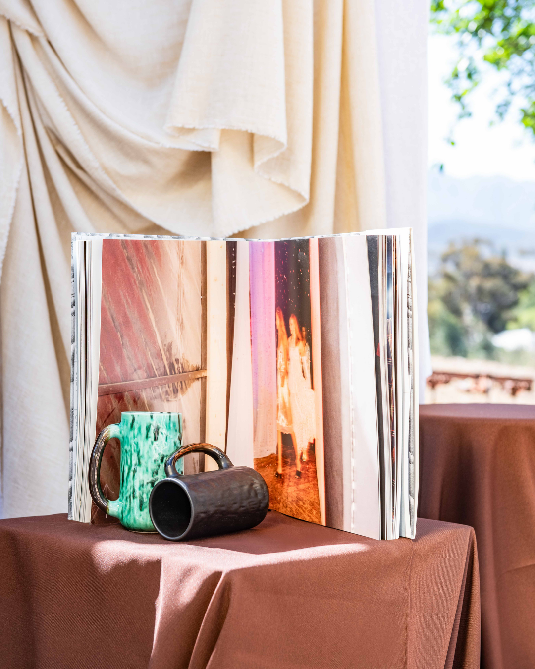 Open photo album on a table with handmade ceramic Mugs in a scenic background