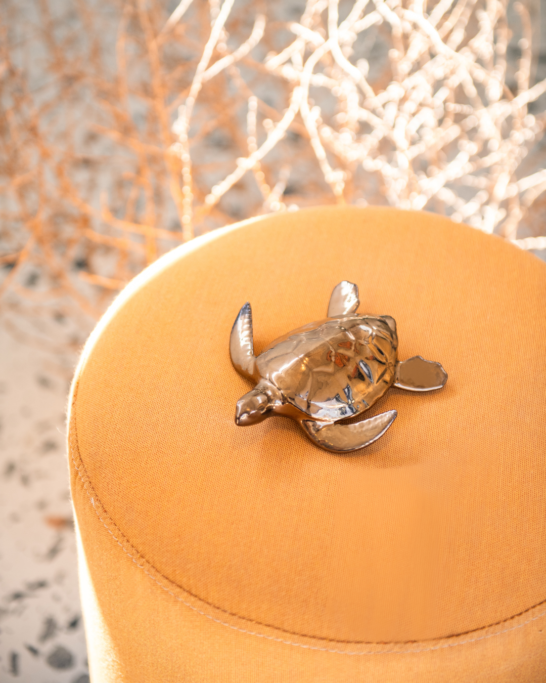 turtle decorative ceramic object in bronze metallic glaze on a yellow cushion with a blurred natural background