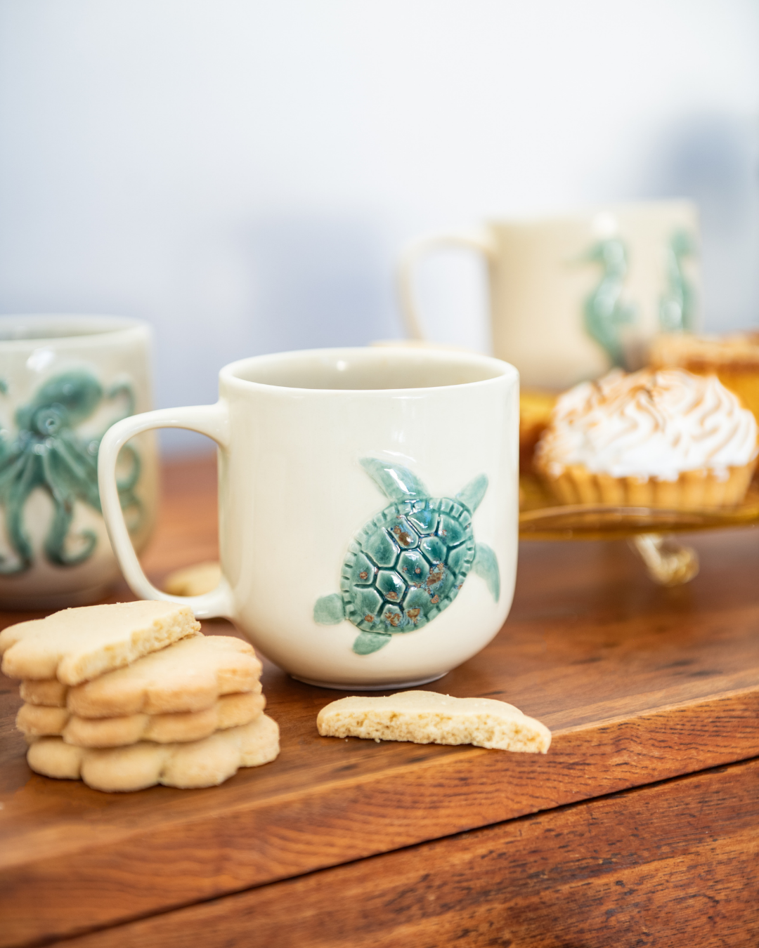 White mug with turtle design on a wooden surface with cookies and a blurred background