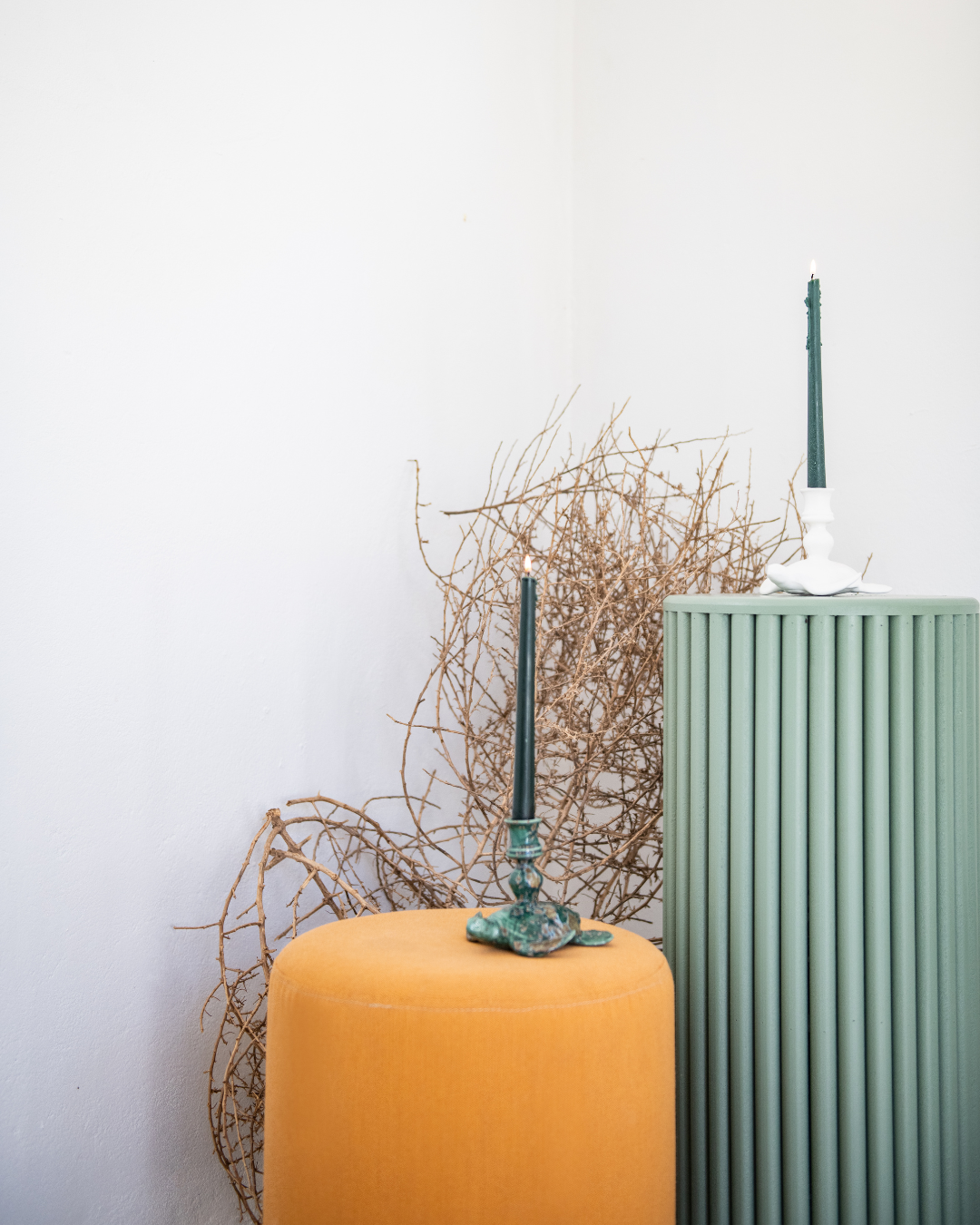 Decorative sea turtle candle stick holders including a green candlestick, on an orange cushion against a white wall. 