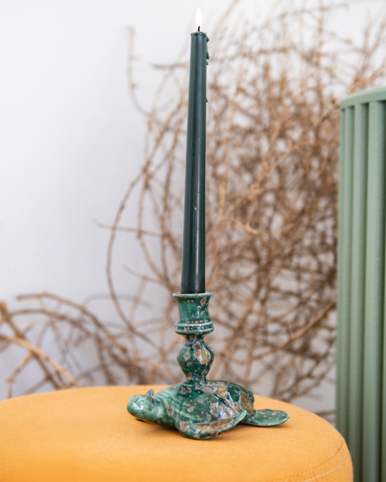 Decorative Crystal Jade sea turtle candle stick holder including a green candlestick, on an orange cushion against a white wall. 