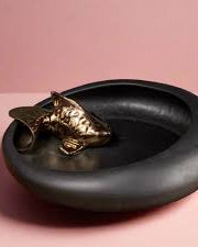 Black dish with a bronze Koi fish figurine on a pink background