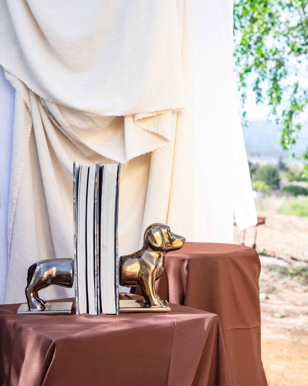 Decorative sausage Dog bookends on a table with a draped curtain and outdoor scenery in the background