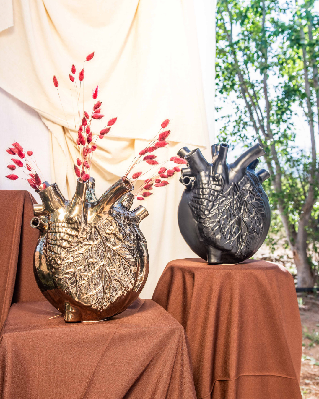 Two decorative vases shaped like human hearts on a brown tablecloth with a natural background.
