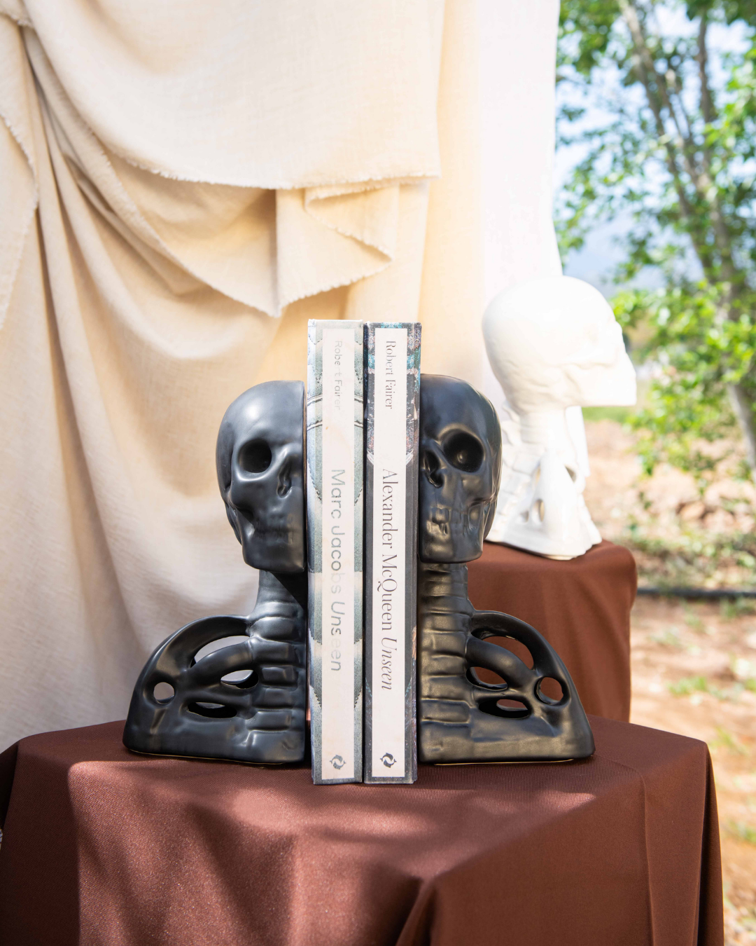 Decorative human skull and spine black bookends with books on a table outdoors
