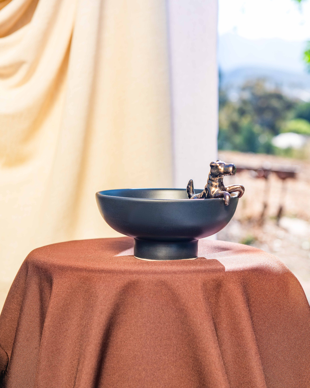 Decorative black bowl with a small figurine on a brown surface, blurred outdoor background