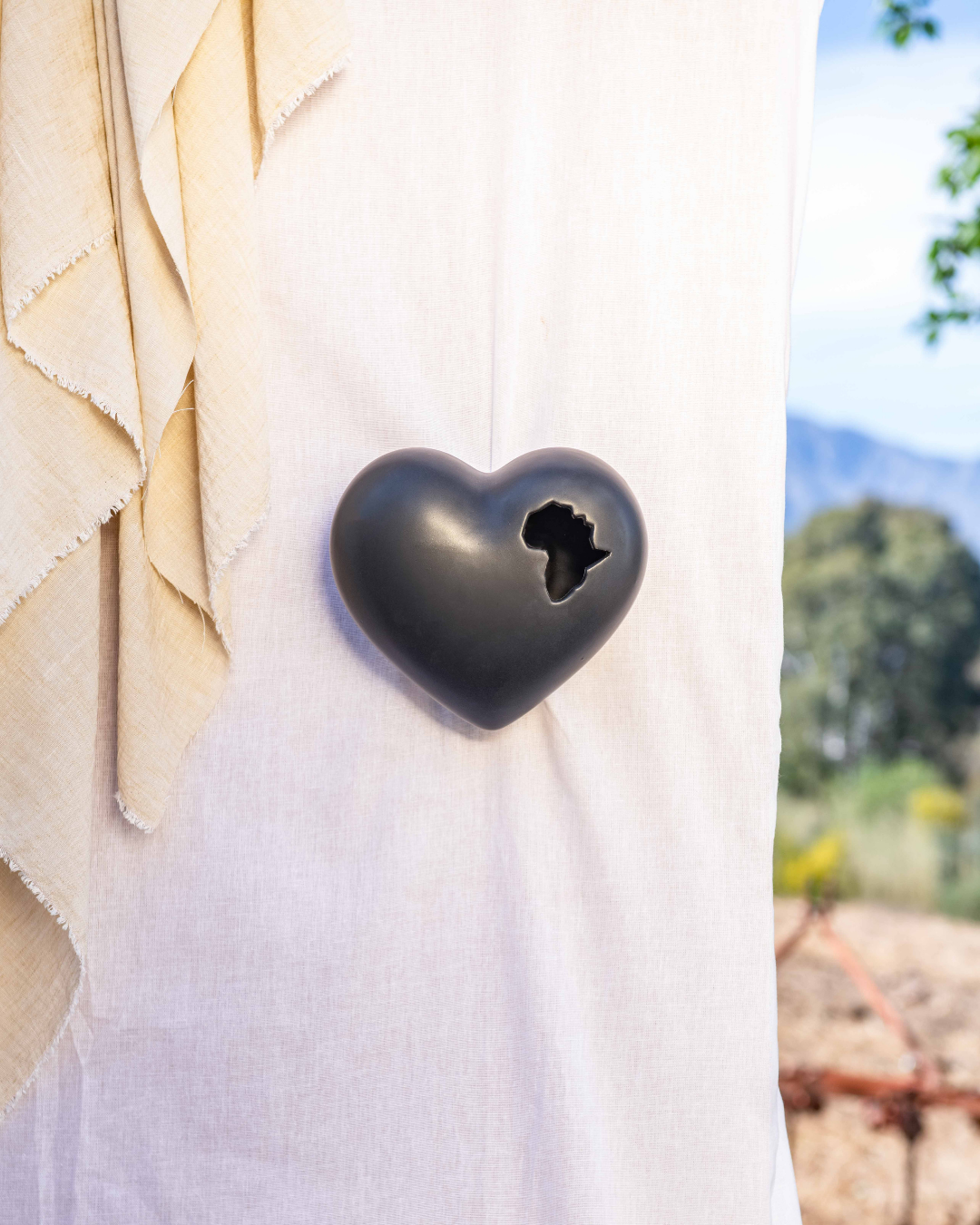 3D Heart-shaped black object with the African content cut out of the ceramic vessel on a white surface with a blurred natural background