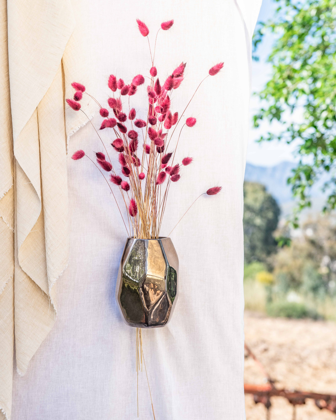Decorative wall vase with red dried flowers against a blurred natural background