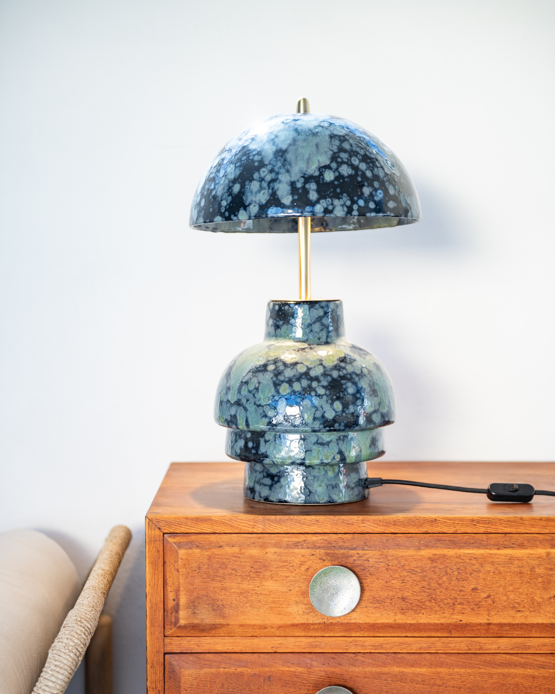 Blue and white speckled table lamp on a wooden cabinet against a white wall