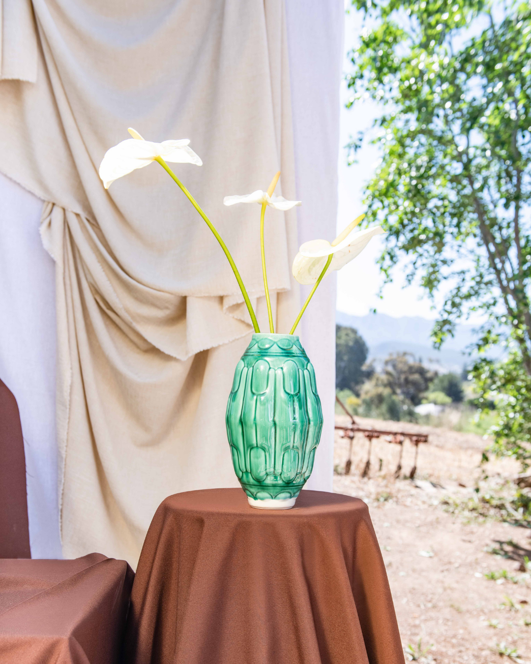 Green textured vase with white flowers on a brown table outdoors