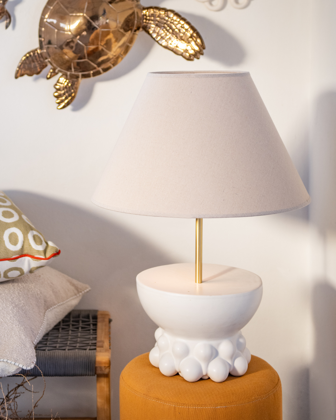 Decorative lamp with a white base and gold accents on an orange stool against a wall with a decorative turtle.