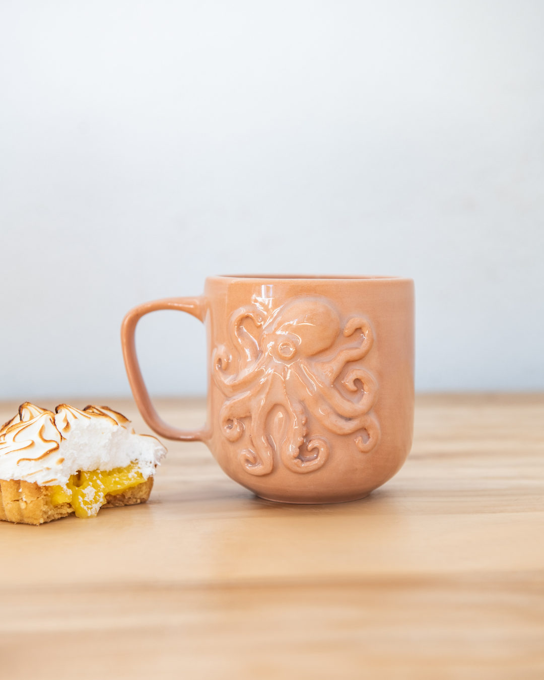 Ceramic mug with octopus design on a wooden surface next to a pastry.