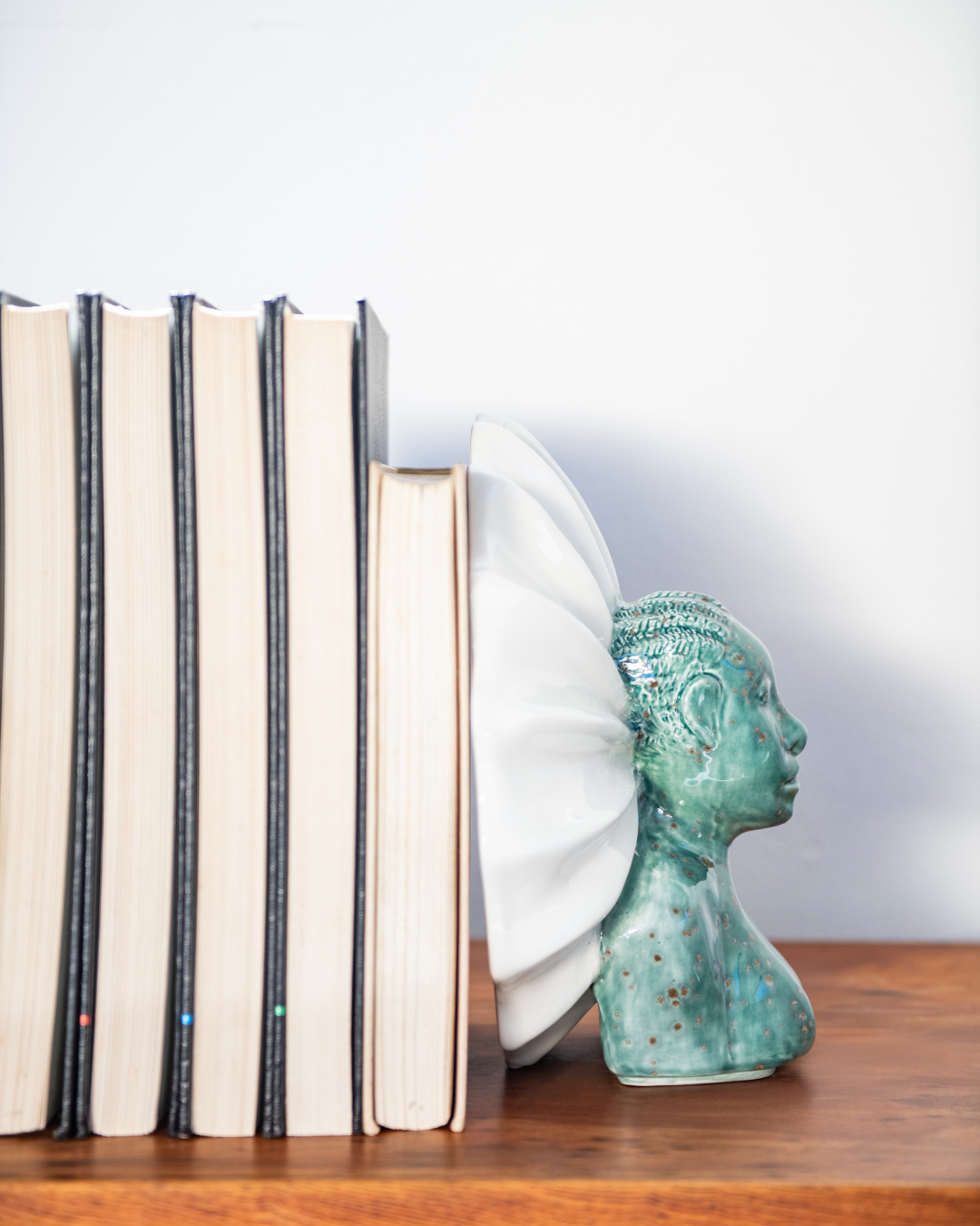 Decorative bookends shaped like a woman's head on a wooden surface with books.
