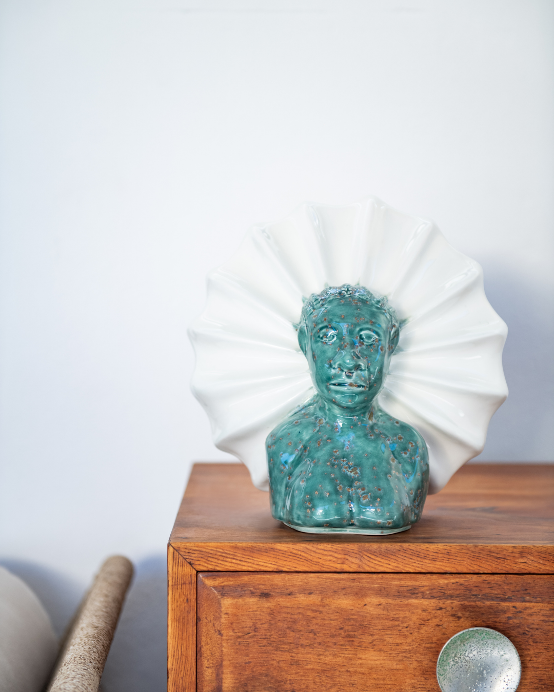 Turquoise ceramic bust on a wooden surface with a white decorative item in the background