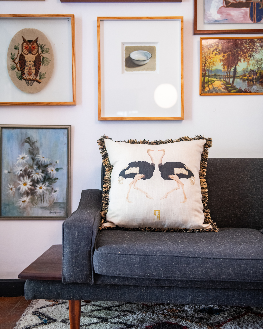 Gray sofa with decorative pillow featuring ostrich birds, framed artwork on the wall.