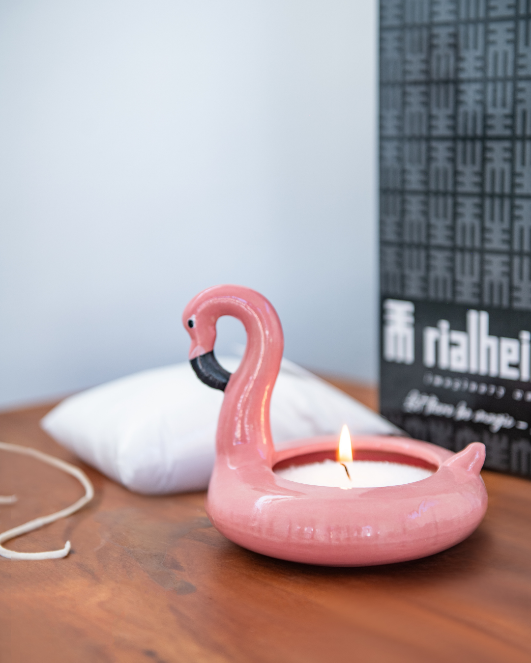 Pink flamingo-shaped candle holder with a lit candle on a wooden surface.