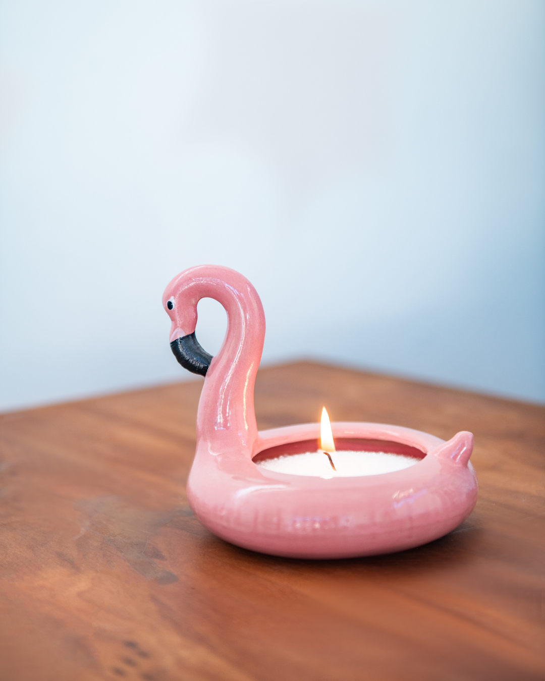 Pink flamingo-shaped candle on a wooden surface with a light blue background