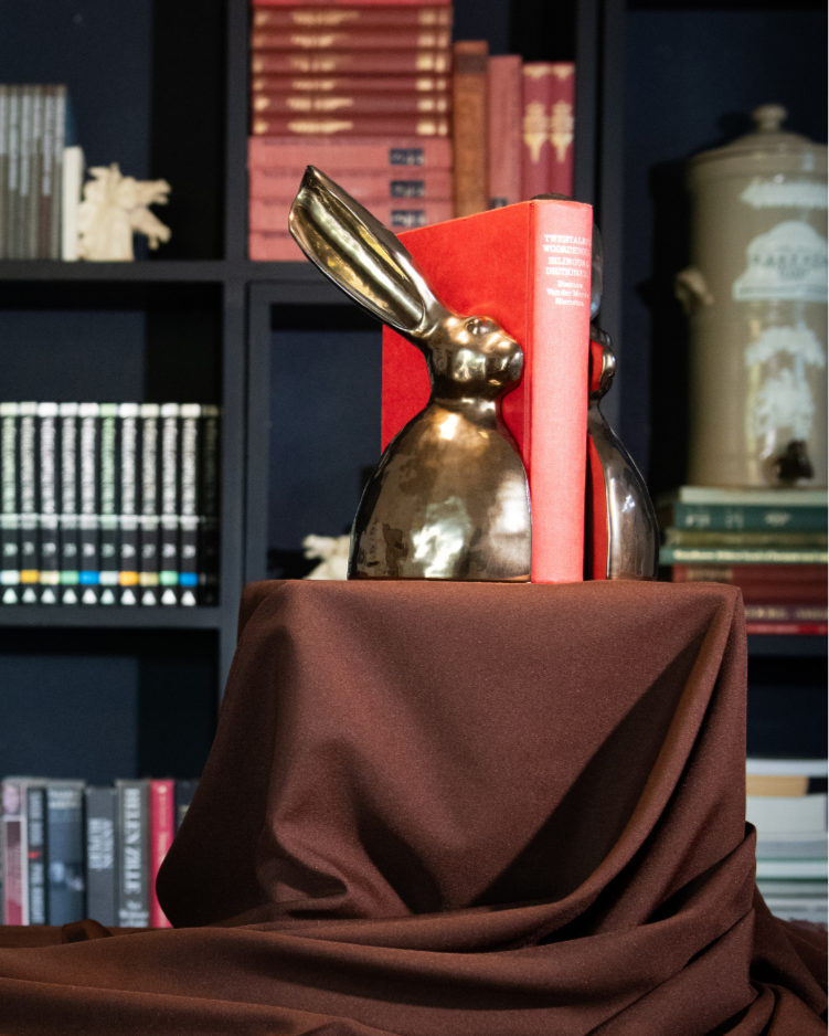 A Riverine Rabbit Book end in white  figurines on a brown cloth with a bookshelf in the background