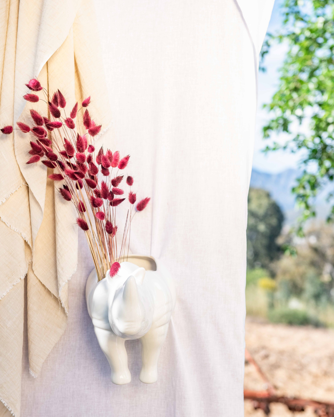 White elephant-shaped vase with red dried flowers against a blurred natural background