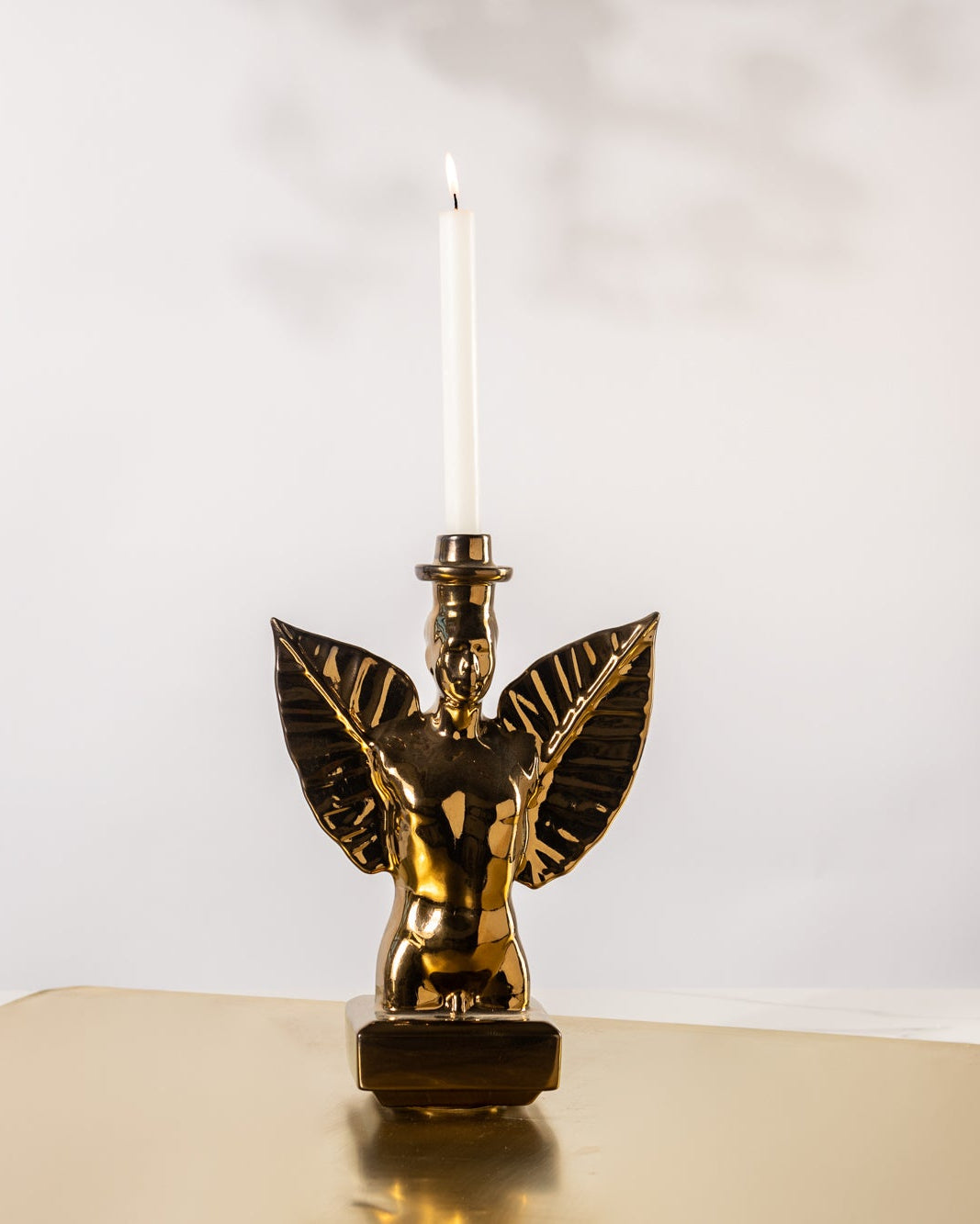 Male Bronzed torso with wings in the shape of leaves and a candle holder on a gold plate in a white room