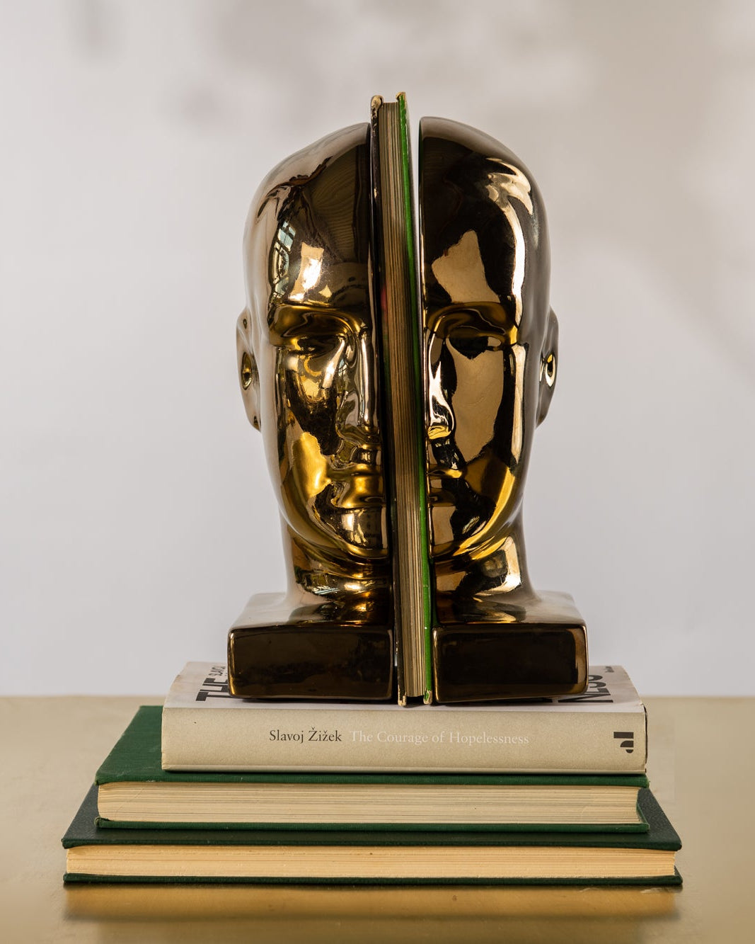 Gold head-shaped bookends on a stack of books with a plain background